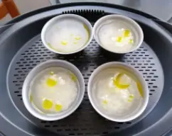 Step <p>En la bandeja varoma, ponga 4 moldes de flan con 25 g de arroz, 50 g de agua, sal y un chorrito de aceite en cada molde, y reserve (medir el arroz y el agua poniendo el molde en el agujero de la tapa y poniendo en marcha el peso)</p> illustration